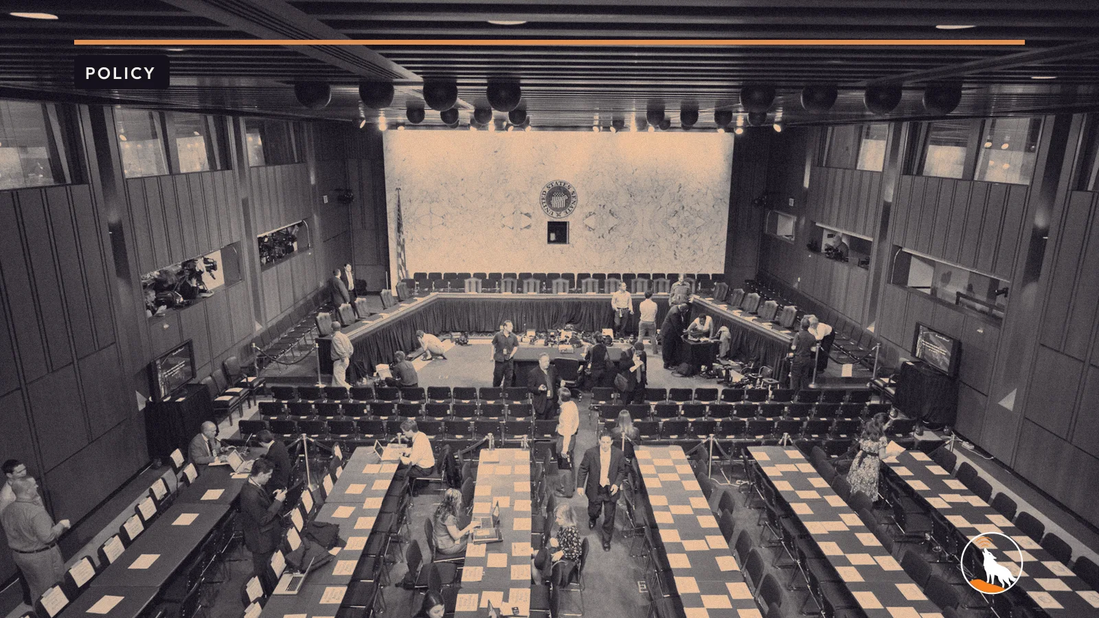 A Senate hearing room, graded navy and orange, with the wolf mark.