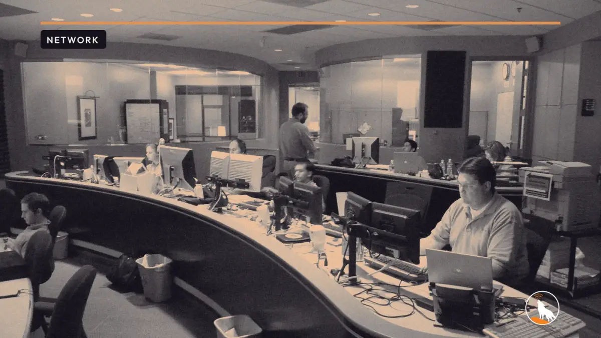 Technicians at consoles in a network operations center, graded navy and orange, with the wolf mark.