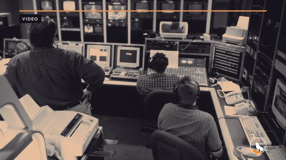A video production crew at a bank of monitors in a studio control room, graded navy and orange, with the wolf mark.