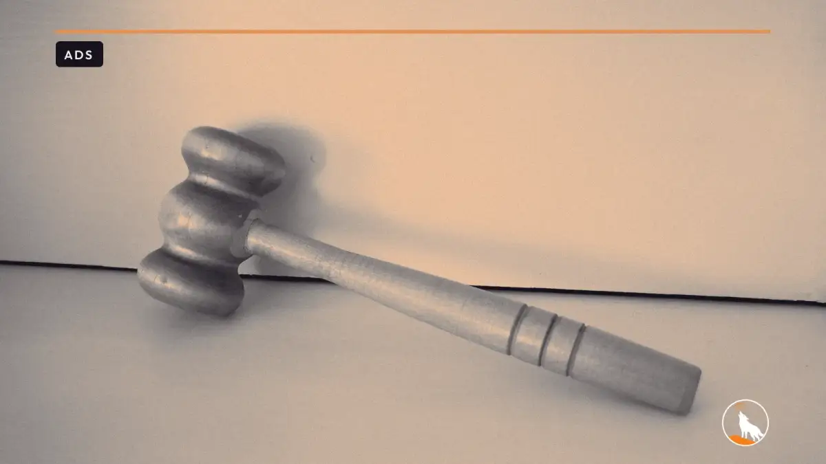 A plain wooden gavel lying on a white shelf against a white wall.