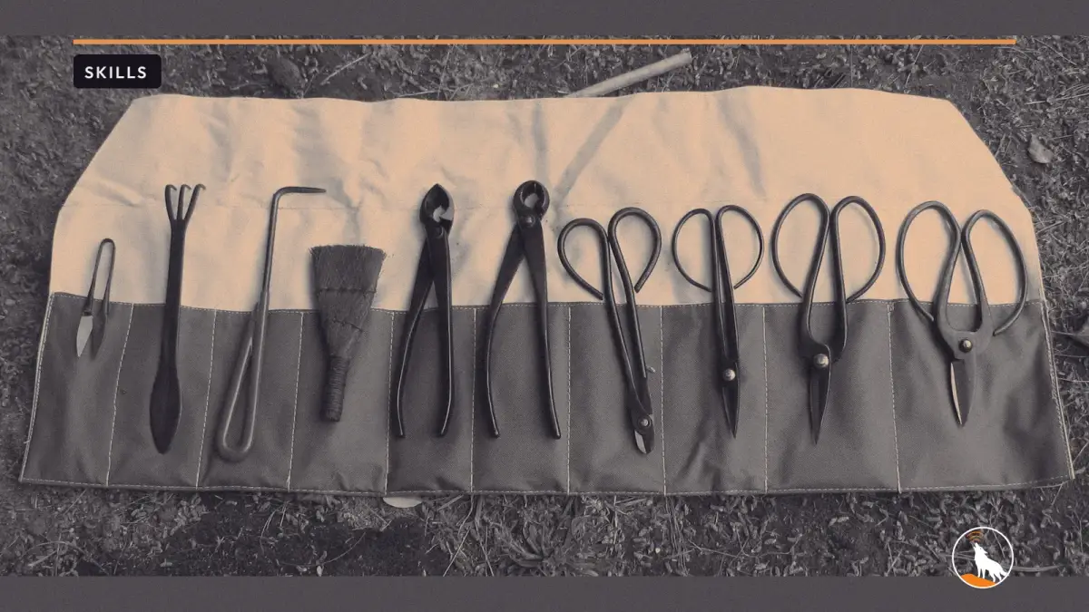 An open canvas tool roll on mossy ground with a row of black bonsai shears, cutters, a rake, a hook and a small brush tucked into its pockets.