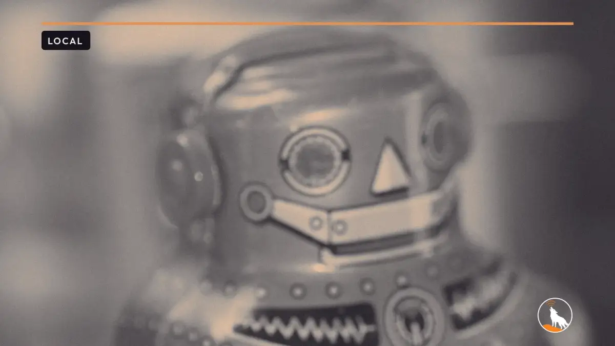 A close-up of a teal vintage tin toy robot with red ears, red eyes and a zigzag chest panel, against a soft yellow background.